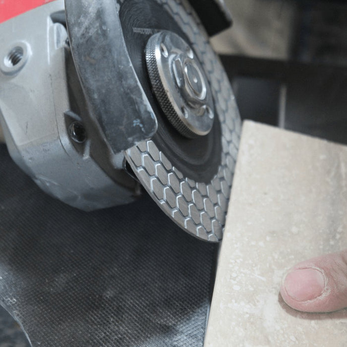 Close-up of a professional tile setter using the RTC E-Z Miter 5" blade to create a smooth, precise miter cut on a porcelain tile, showcasing the blade's unique honeycomb design and extra tall rim in action.