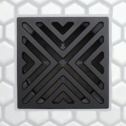 Square matte black drain grate with chevron V openings and dark surrounding channels
