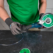 Person using a diamond grinding machine on a black surface with a green shirt and gloves.